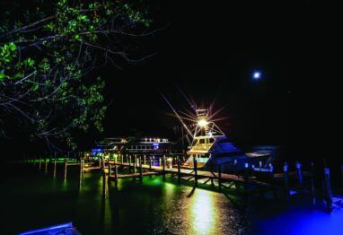 A dock at night lit by the light from a ship's tower.
