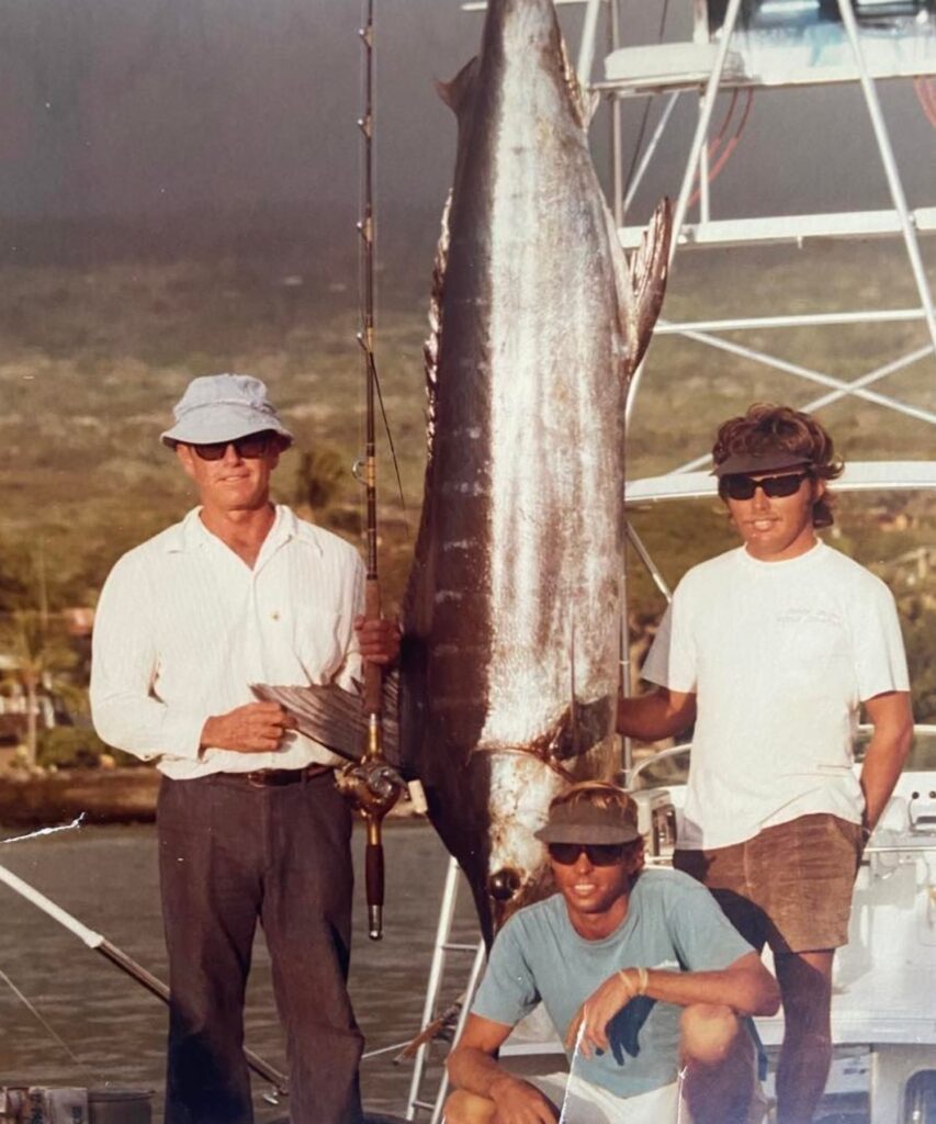 3 guys standing next to a hanging marlin