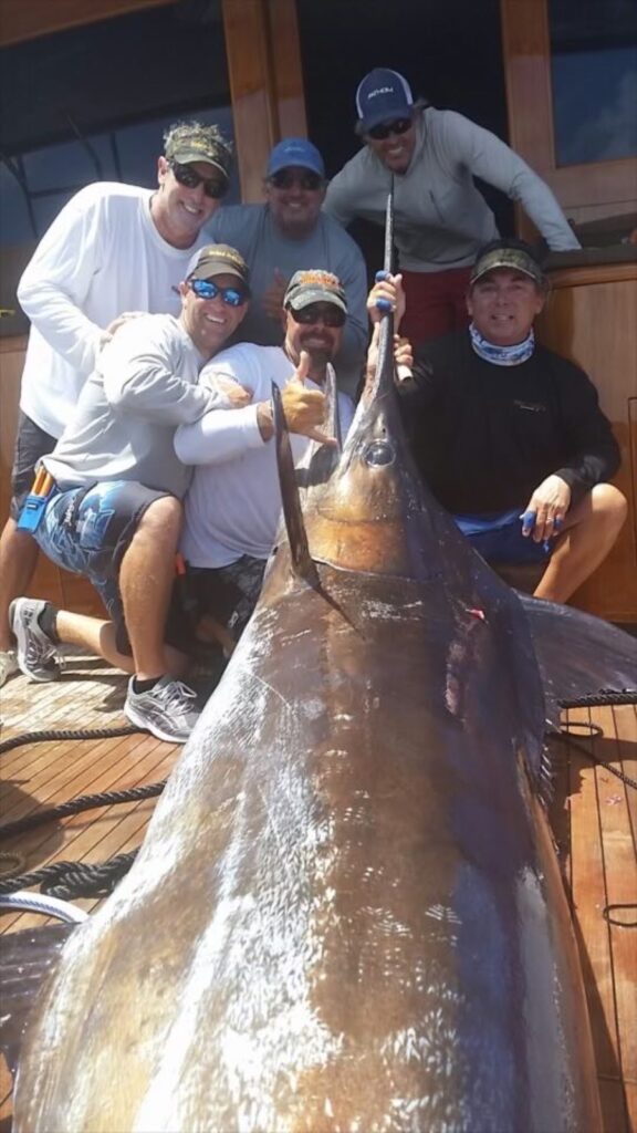 Capt Ray Rosher with a group in the back of a boat holding a big marlin 