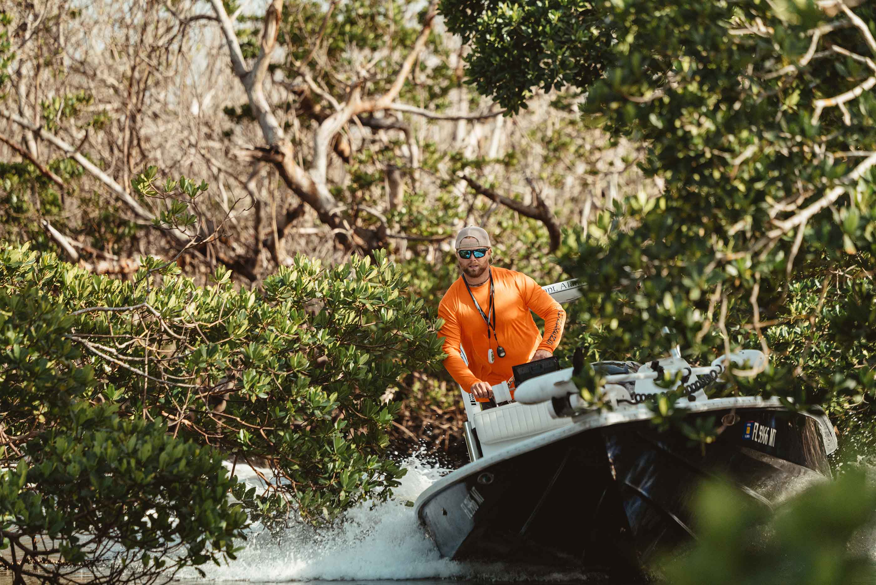 Angler Sun Protection by grundens, man in orange shirt driving a boat