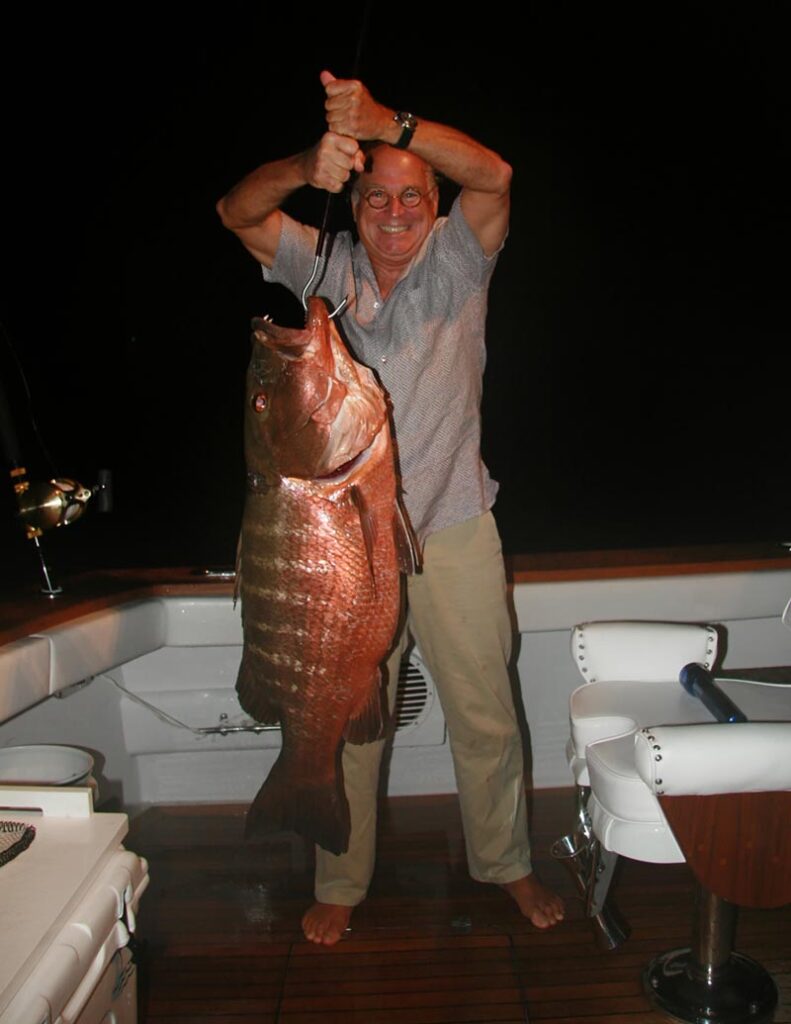 Jimmy Buffett holding up a cubera snapper at night off the back of the boat