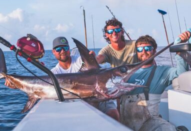 3 guys fishing holding a swordfish after catching it with an electric fishing reel
