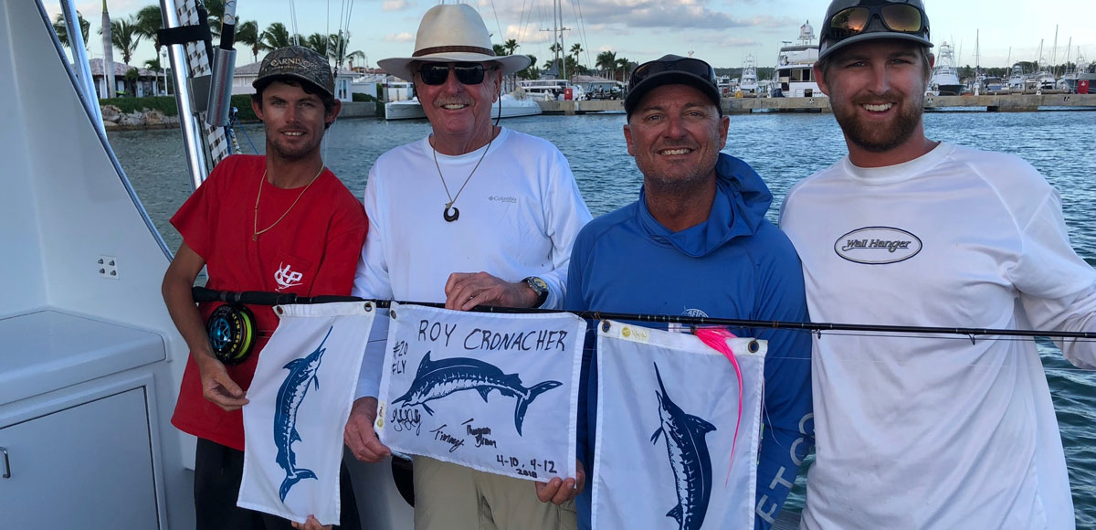 4 crew members holding a fly rod with 3 marlin release flags