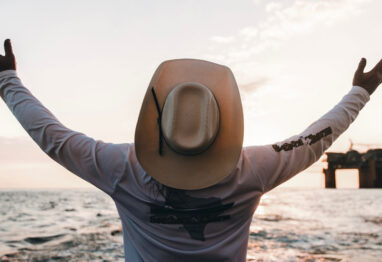 a man in a cowboy looking at a oil rig in the gulf of mexico in a cowboy hat.