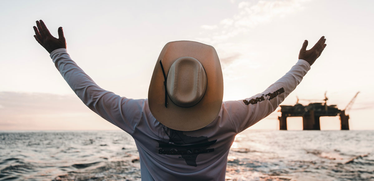 a man in a cowboy looking at a oil rig in the gulf of mexico in a cowboy hat.