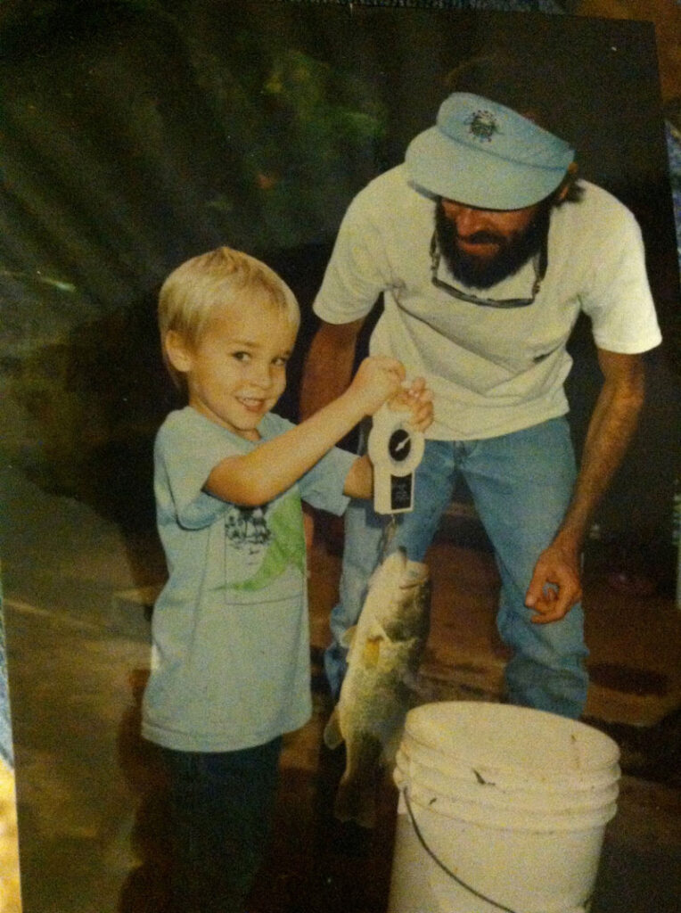 a boy and his father looking on as the boy weighs a bass fish