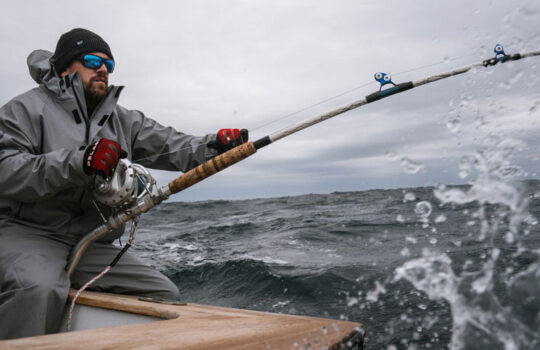 a man fighting a fish with a large fishing rod in foul weather