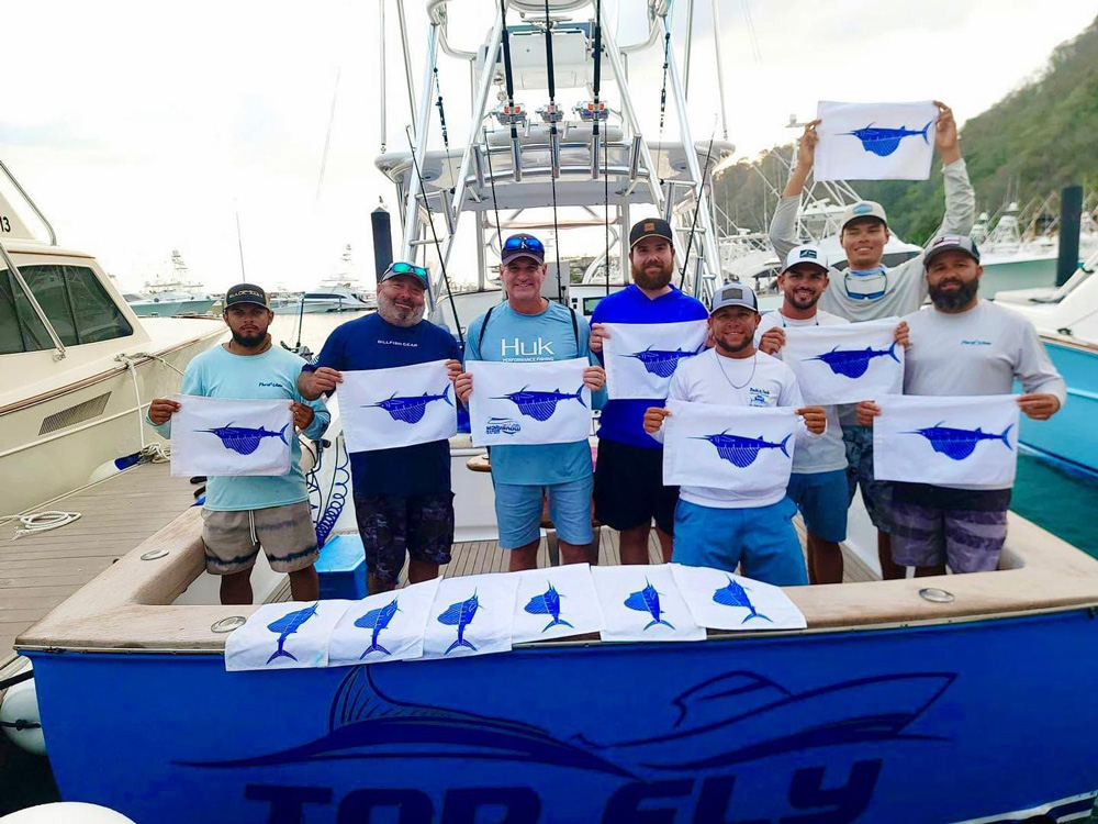 top fly boat with a crew holding several white and blue sailfish release flags