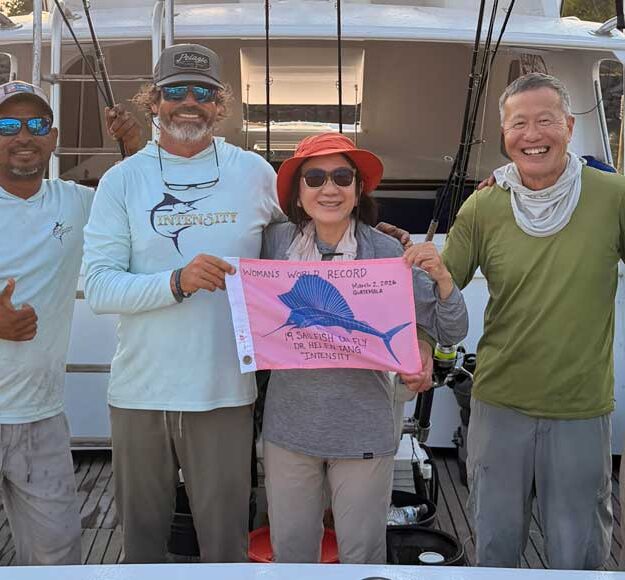 Helen Tang Sets New Sailfish Fly Record with 19 Releases holding thepink flag with the crew in this image