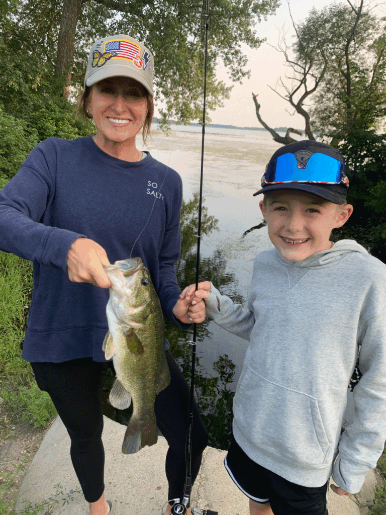 Carly Hysell from Garmin holding a bass with her son next to her