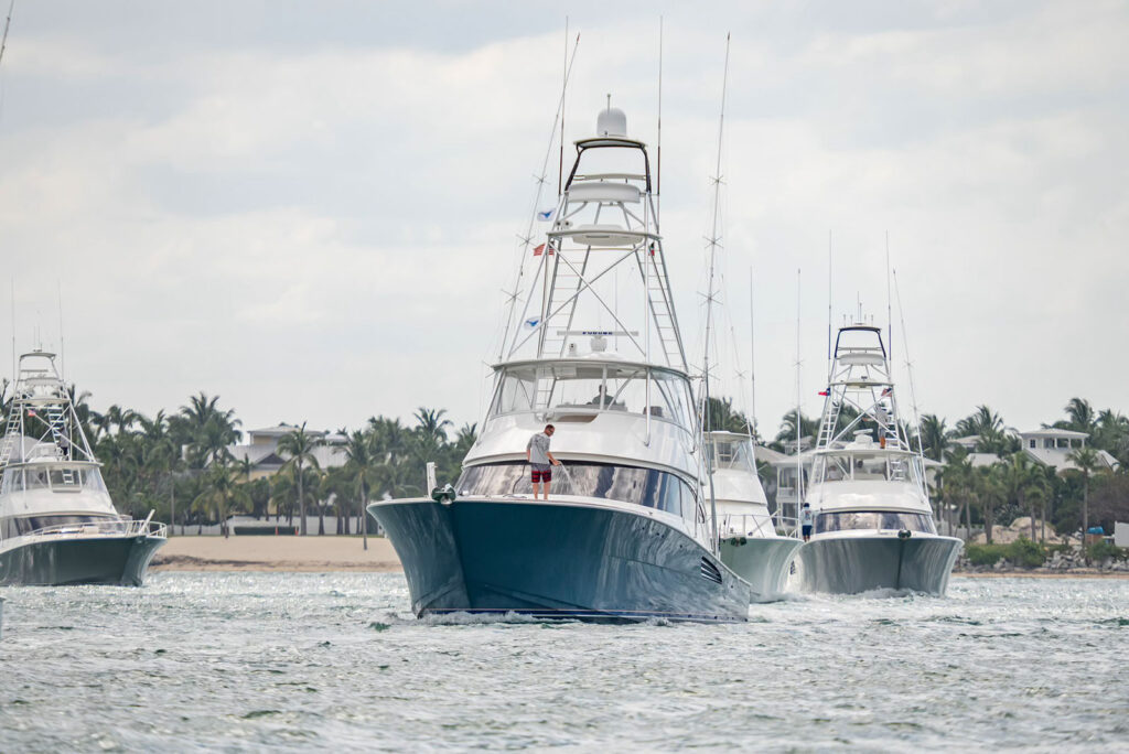Crew member hosing down the bow of a sportfishing boat underway as other tournament boats follow
