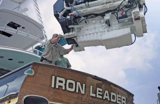 Technician guides a marine diesel engine being lifted out of the sportfishing yacht Iron Leader at Safe Harbor Jarrett Bay.