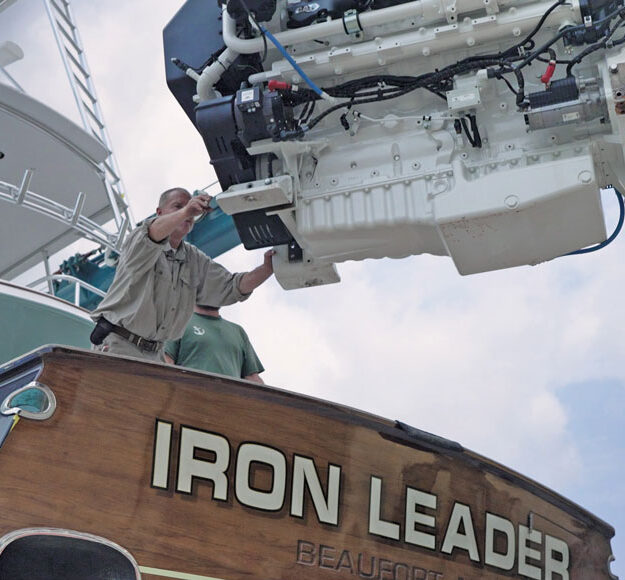 Technician guides a marine diesel engine being lifted out of the sportfishing yacht Iron Leader at Safe Harbor Jarrett Bay.