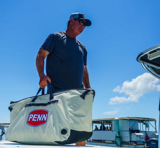 a fisherman carrying the PENN Ballast insulated catch cooler with side drain plug and Hypalon drag pads