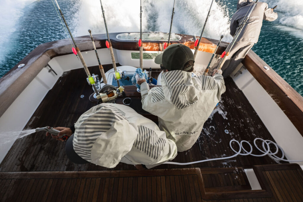 Overhead view of crew in Simms Rip Line Pro jackets washing down a teak cockpit while the boat runs offshore