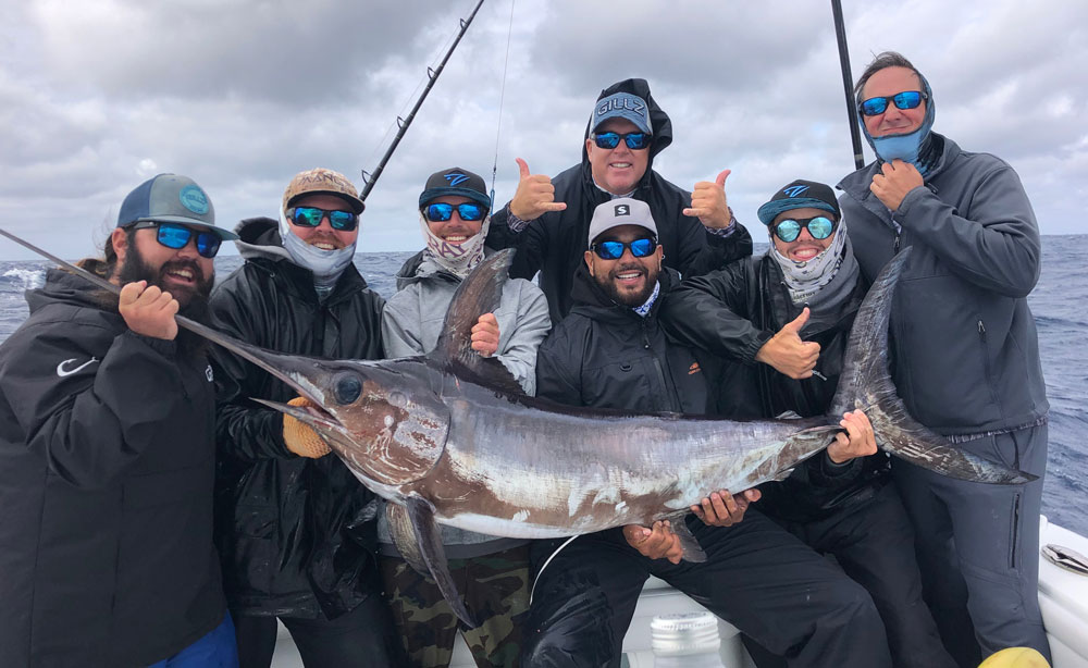 7 people taking a picture with a swordfish on the boat